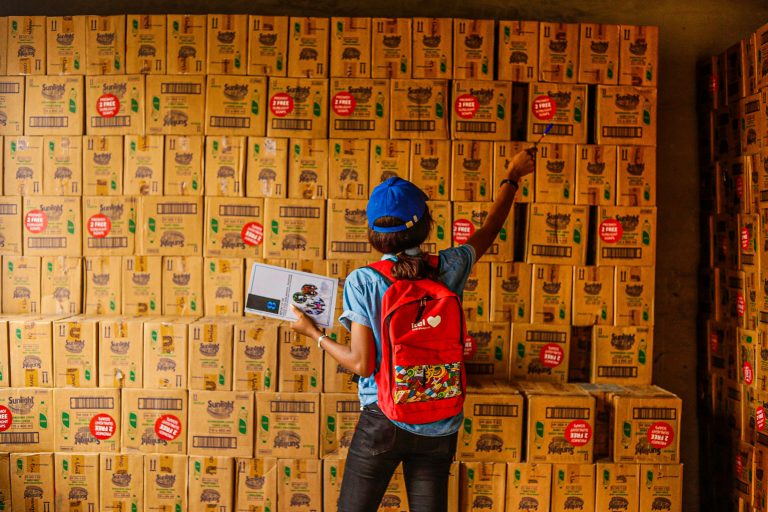 Woman organizing inventory with a clipboard in a warehouse full of boxes.